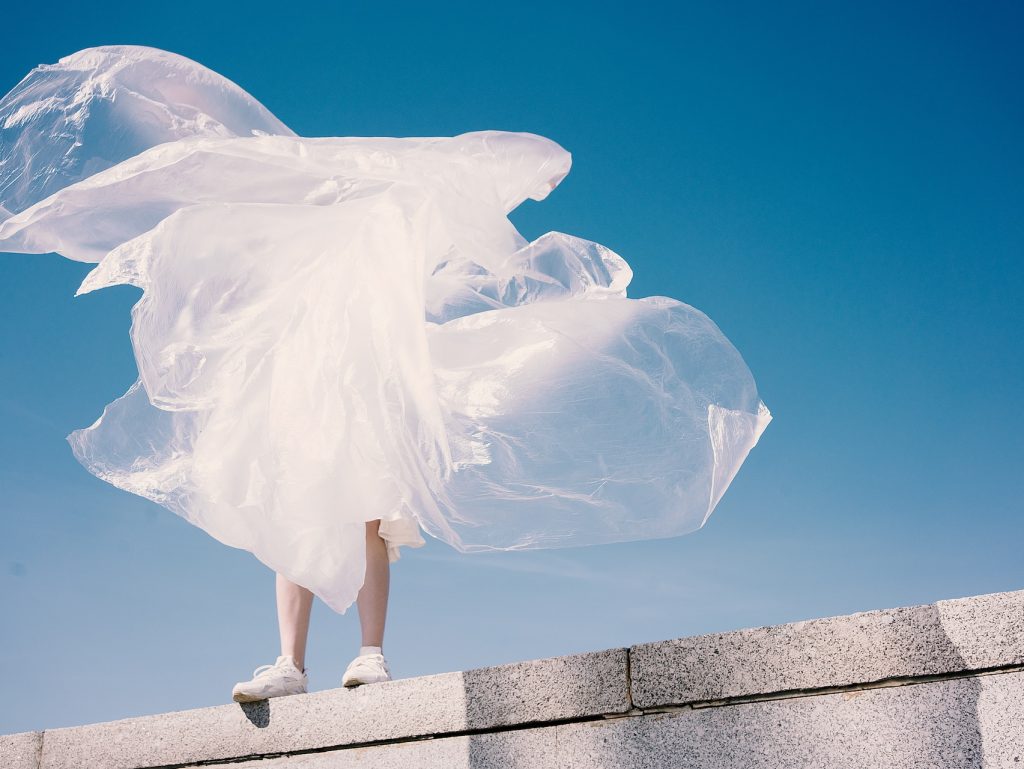 a person standing on a concrete wall with a big nylon sheet covering his/her body not tightly but loosely with the wind